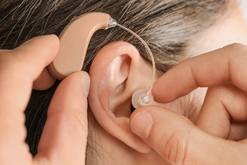 Close-up of a person fitting a behind-the-ear hearing aid, with fingers adjusting the clear earpiece into the ear canal.